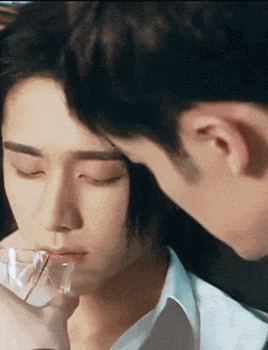 a man is kissing another man 's forehead while holding a glass .