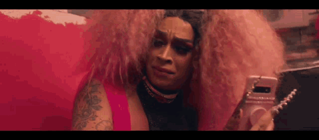 a drag queen with pink hair is taking a picture of herself on her phone .