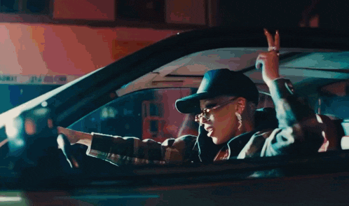 a man wearing a hat and sunglasses is driving a car