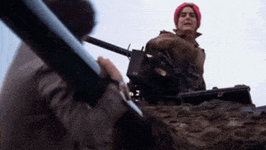 a woman in a red hat is sitting in a tank with a gun .