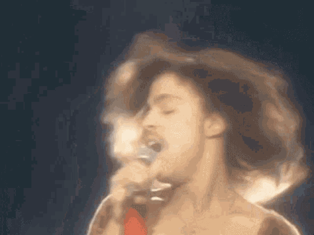 a close up of a person singing into a microphone with their hair blowing in the wind .