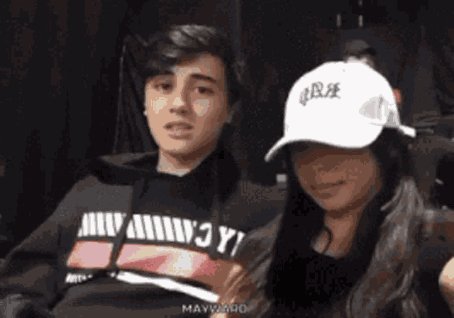 a boy and a girl are sitting next to each other and the girl is wearing a white hat that says " love "