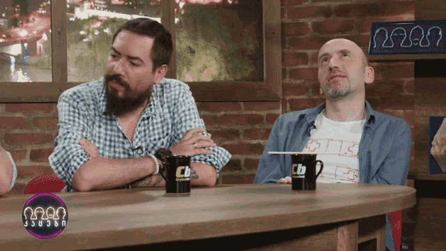 two men sit at a table with a cup that says cb