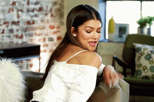 a woman in a white off the shoulder top is sitting on a couch in a living room