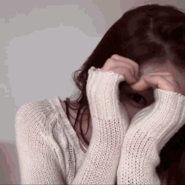 a woman wearing a white sweater covering her face with her hands