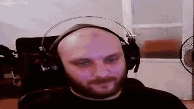a bald man with a beard wearing headphones and a fan in the background .