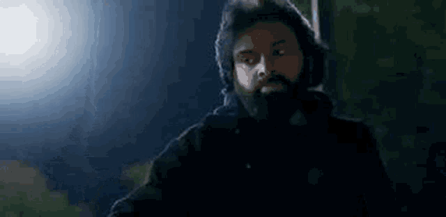 a man with a beard is wearing headphones and a black jacket in the dark .