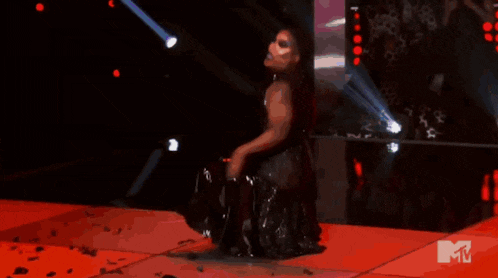 a woman in a black dress is dancing on a stage with a mtv logo behind her