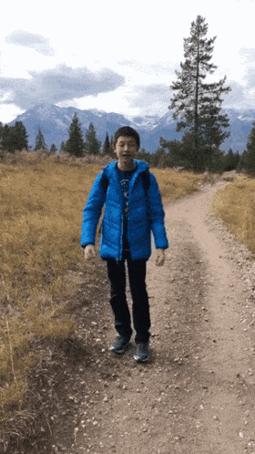 a boy in a blue jacket is walking down a dirt road