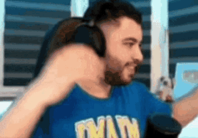 a man wearing headphones and a blue shirt is standing in front of a window .