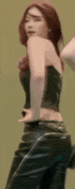 a woman in a black top and black leather pants is dancing on a green background .