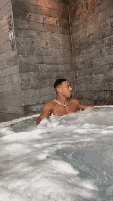a shirtless man is sitting in a hot tub with a few showers behind him
