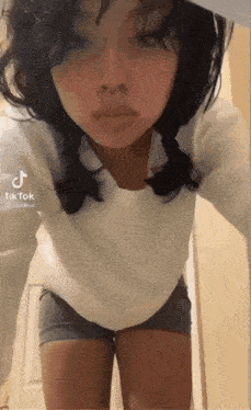 a woman in shorts and a white shirt is standing in front of a door with tiktok written on the bottom