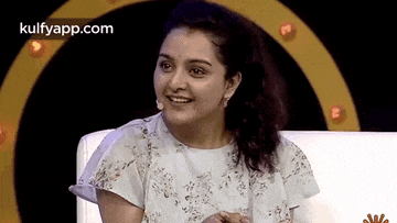 a woman is smiling while sitting on a couch in front of a microphone .