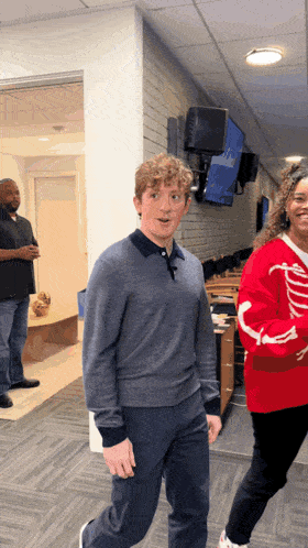 a man in a grey sweater is standing next to a woman in a red sweater with ribs on it