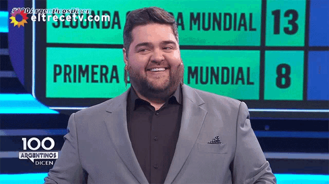 a man in a suit is smiling in front of a scoreboard that says primera mundial