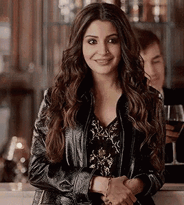 a woman in a leather jacket is shaking hands with a man in a bar while holding a glass of wine .
