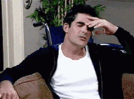 a man in a white shirt is sitting on a couch with his hand on his forehead .