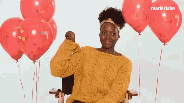 a woman in a yellow sweater is surrounded by red balloons and confetti with the marie claire logo in the background