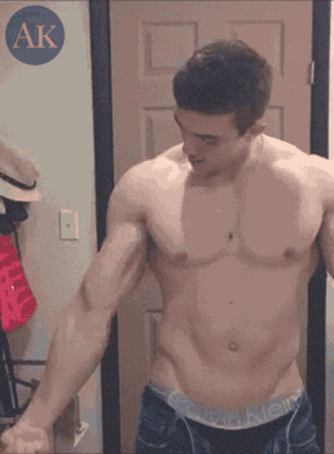 a shirtless man is flexing his muscles in front of a mirror with the letter ak in the corner