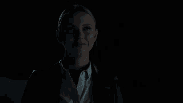 a woman is smiling in the dark while wearing a black jacket and a white shirt .