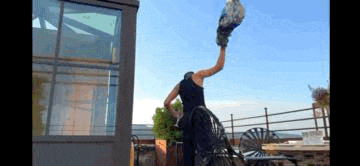 a man in a black tank top is standing on a rooftop holding a bird in his hand .