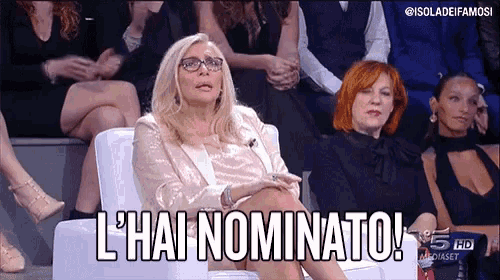 a woman is sitting in a chair with her legs crossed and says l ' hai nominato .