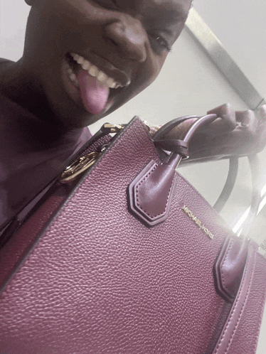 a woman sticking her tongue out while holding a michael kors bag