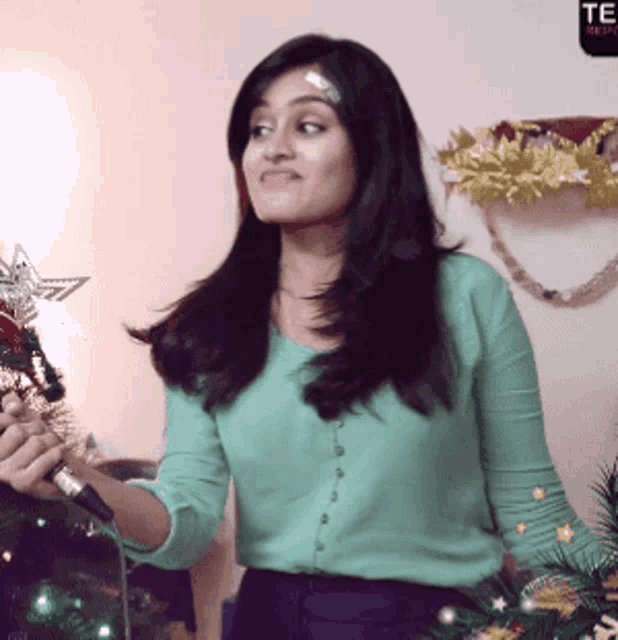 a woman in a green shirt stands in front of a christmas tree with a star on top