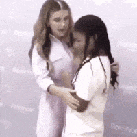 two women are hugging each other while standing next to each other in front of a wall .