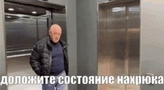 a bald man in a black jacket is standing in an elevator with russian writing on it .