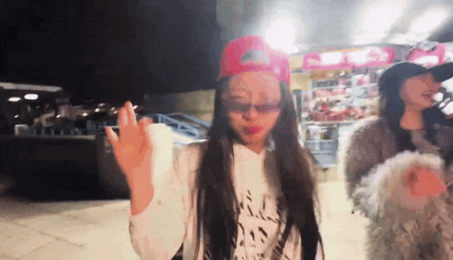 a woman wearing a red hat and sunglasses waves her hand