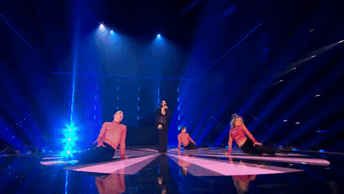 a woman singing on a stage with a group of dancers
