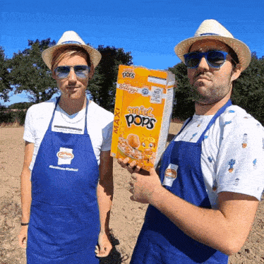 two men wearing blue aprons holding a box of honey pops