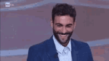 a man with a beard is smiling while wearing a blue suit .