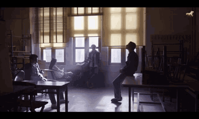 a man sits on a desk in a classroom with a yellow blind on the window