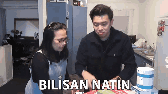 a man and a woman are standing in a kitchen with the words " bilisan natin " on the screen