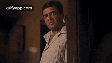 a man in a striped shirt is peeking out of a doorway and making a funny face .
