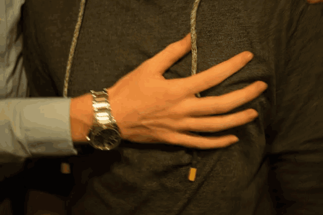 a man wearing a watch on his wrist holds his hand on his chest