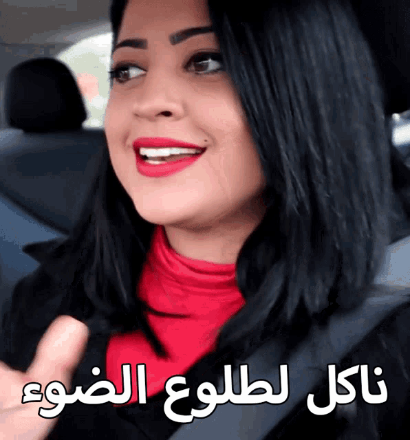 a woman wearing red lipstick is smiling in a car with arabic writing behind her