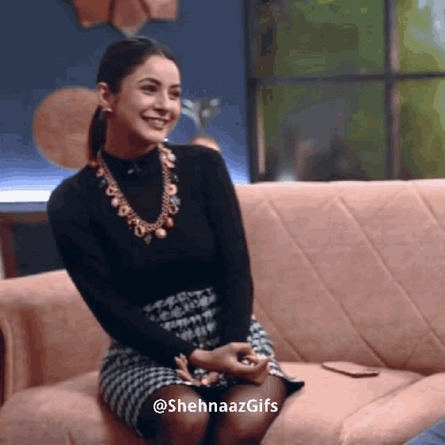 a woman is smiling while sitting on a couch with the hashtag shehnaazgifs at the bottom