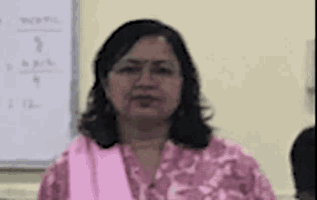 a woman in a pink shirt is standing in front of a white board in a room .