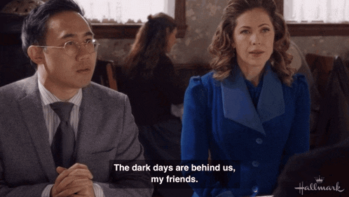 a man and a woman sit at a table with the words " the dark days are behind us my friends "