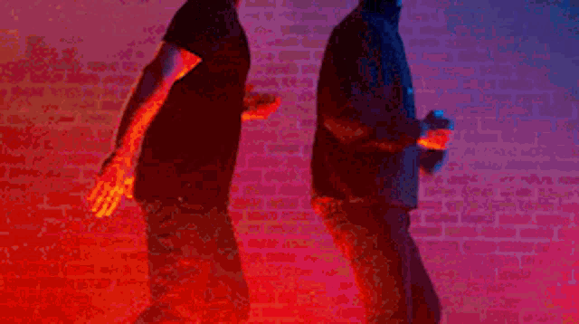 a couple of men are running in front of a brick wall .