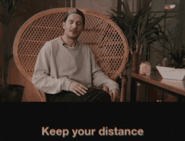 a man sits in a wicker chair with the words keep your distance on the bottom