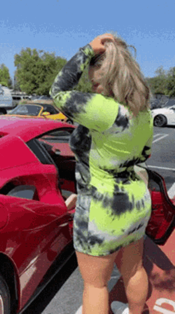 a woman in a neon green tie dye dress is standing next to a red sports car