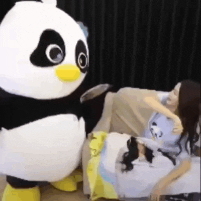 a panda mascot is standing next to a woman sitting on a bed .