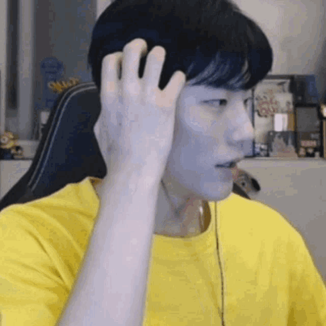 a man in a yellow t-shirt is sitting in a chair and touching his head .