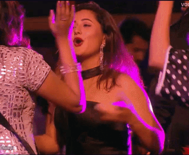 a woman in a black dress is dancing in a club with purple lights behind her .