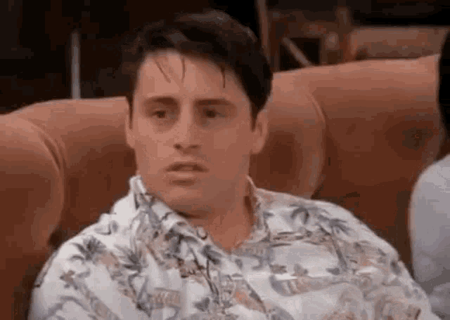 a man is sitting on a couch wearing a floral shirt and making a funny face .